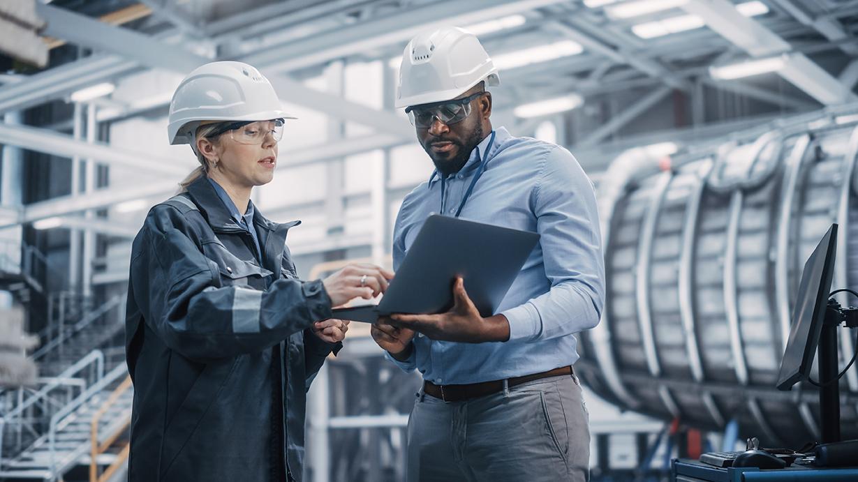 Two industry engineers standing inside a manufacturing factory using EAM system, The Asset Guardian (TAG), on a digital tablet device.