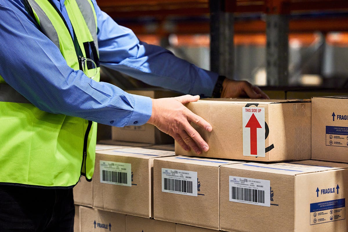 Warehouse worker organizing inventory stacking boxes with proper handling instructions for optimal inventory management registered within The Asset Guardian EAM, CMMS.